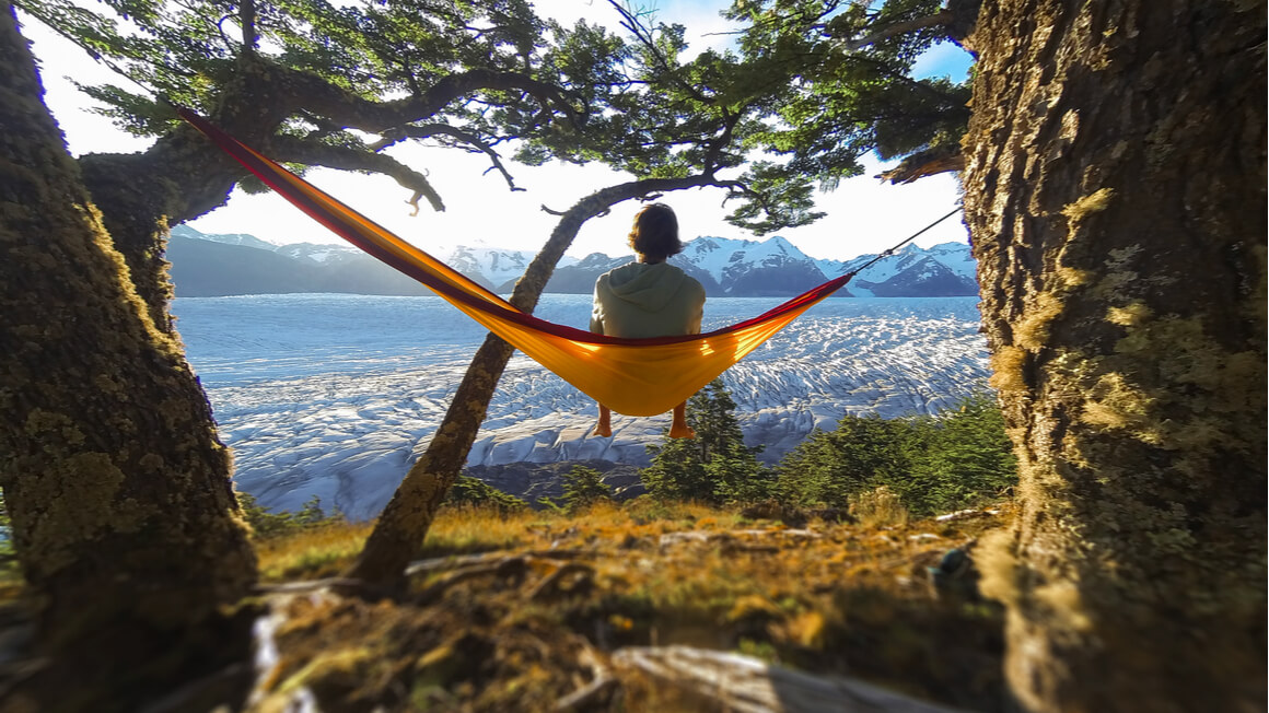 person sitting in a camping hammock overlooking a view below