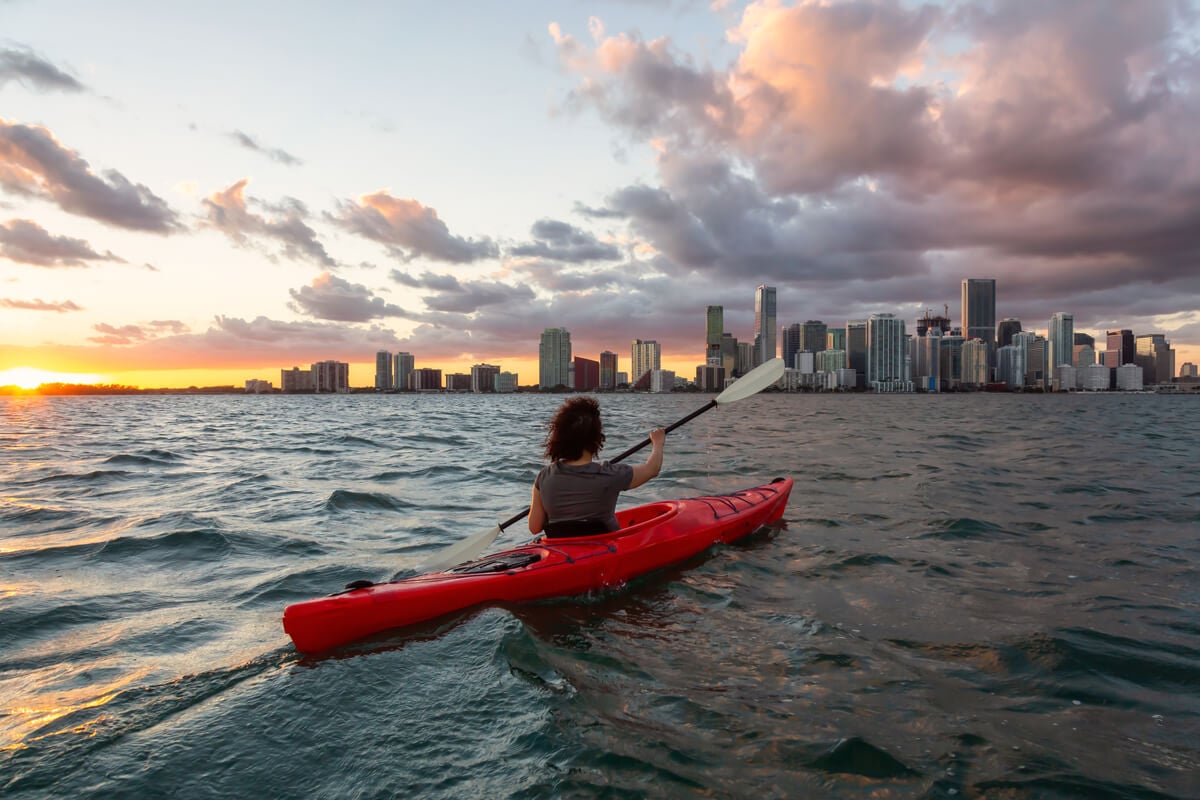 woman kayaking in water in front of miami skyline