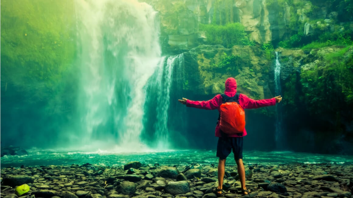 guy in red outfit standing in front of a waterfall