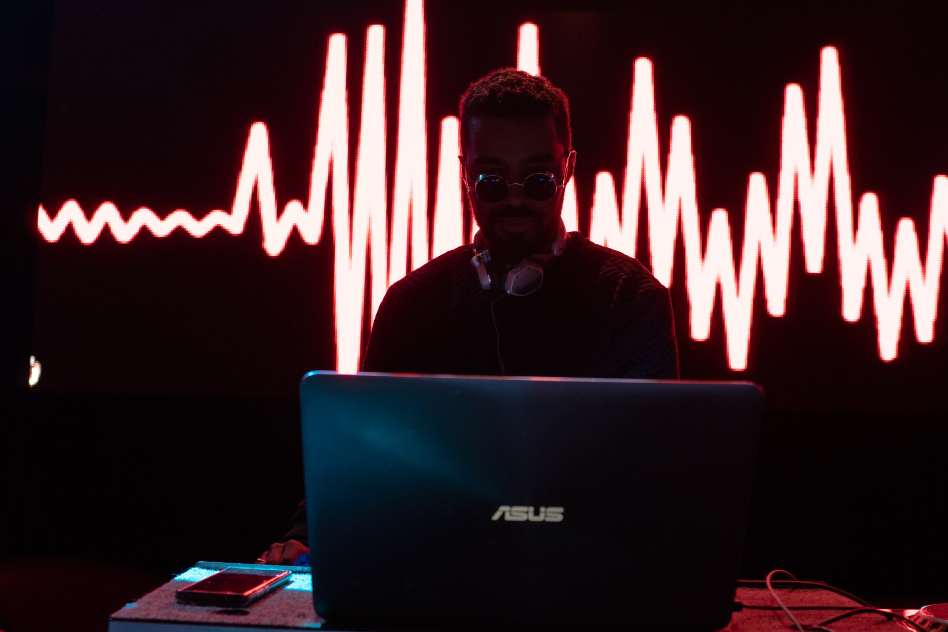 guy djing at a dark club with red heart beat graphic behind him