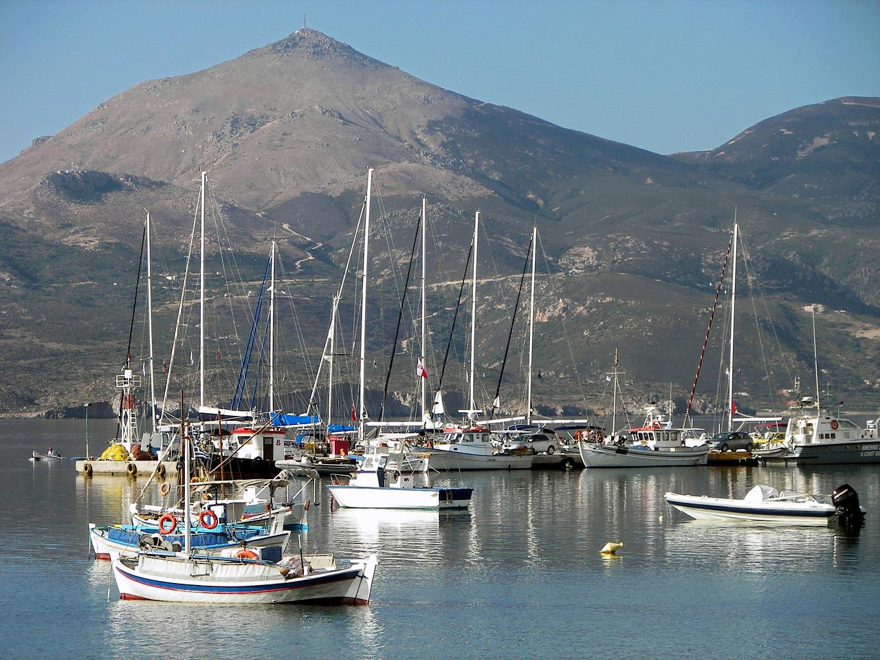 Lots of sail boats on the water with mountains behind