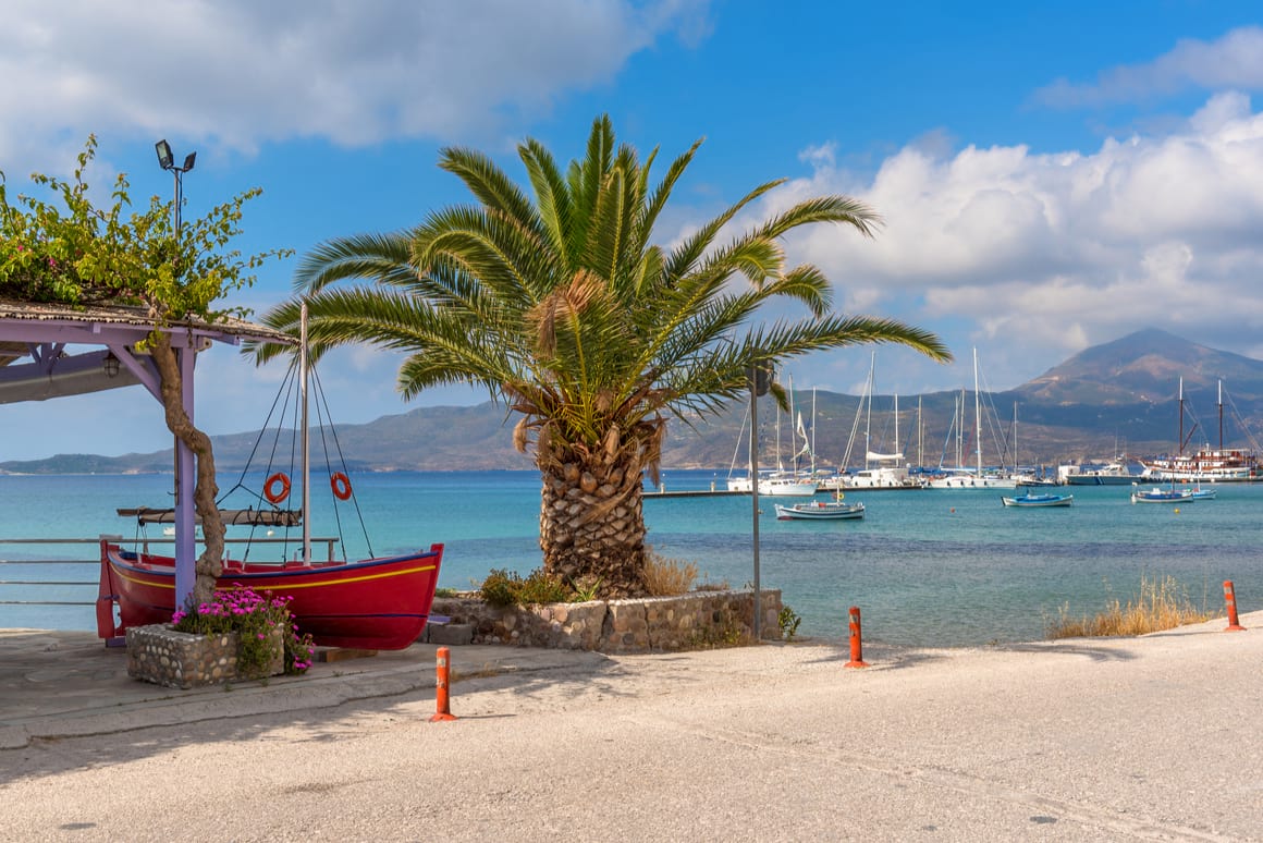 View of the beautiful blue sea with a palm tree in the foreground and sailboats and mountains behind.