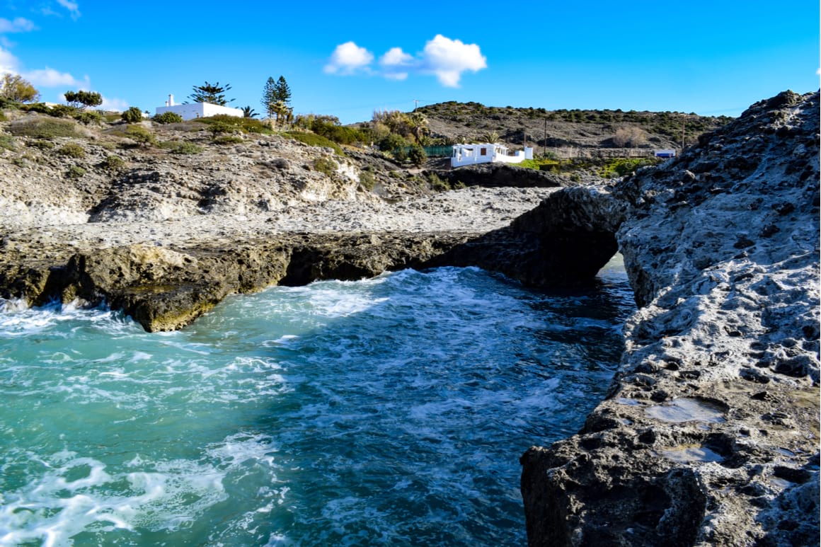 Rocky cove with white wash water. A couple of white, greek houses in the background. 