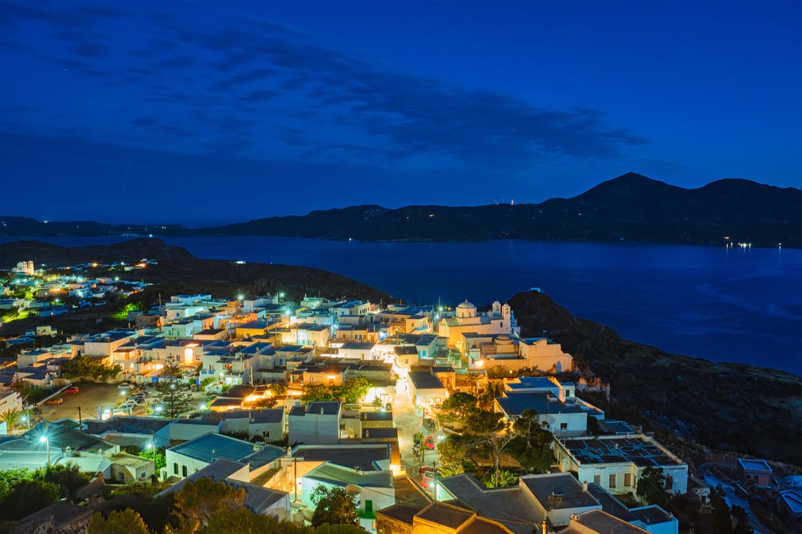 Night time view of Plaka with the ocean and mountains in the background.