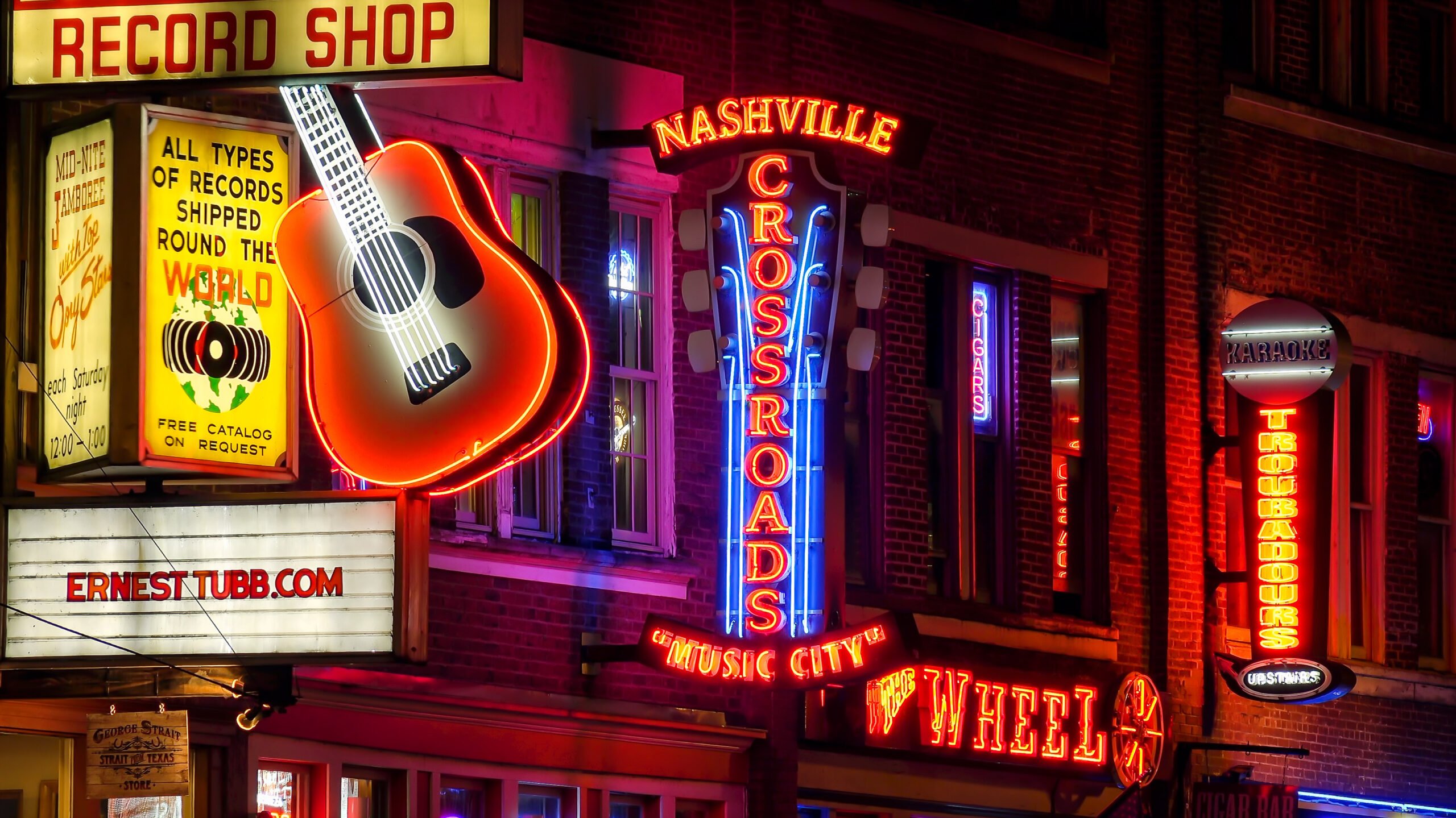 neon red and blue signs next to a huge guitar lit up on a street in nashville 