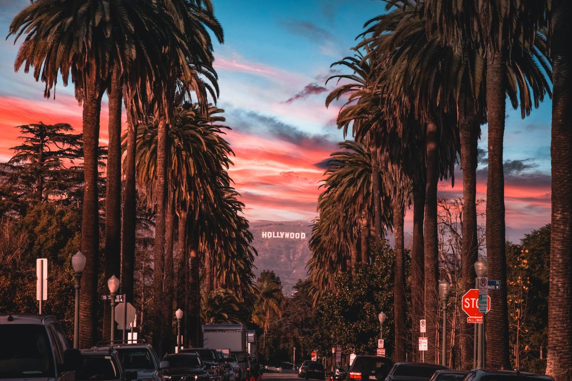 sunset with palm trees lining the street and hollywood sign in the distance