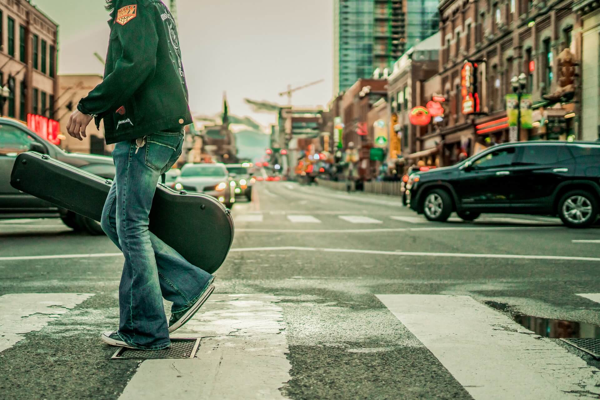 Person carrying guitar case walking across street crosswalk