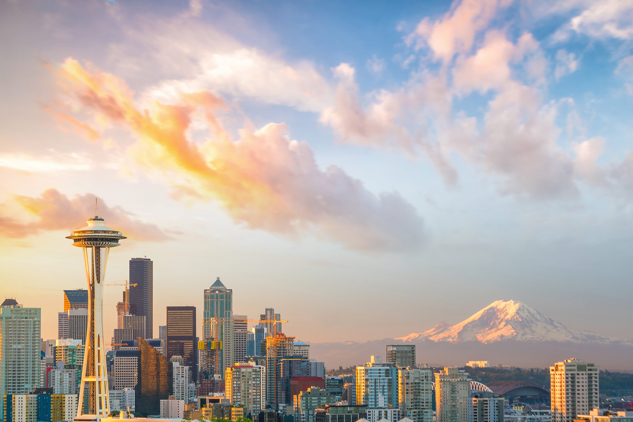 Seattle city skyline, with snowy mountain peaking up behind the city at sunset