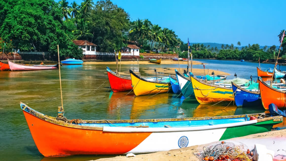 colorful boats in the sea in goa with traditional seaside homes behind them