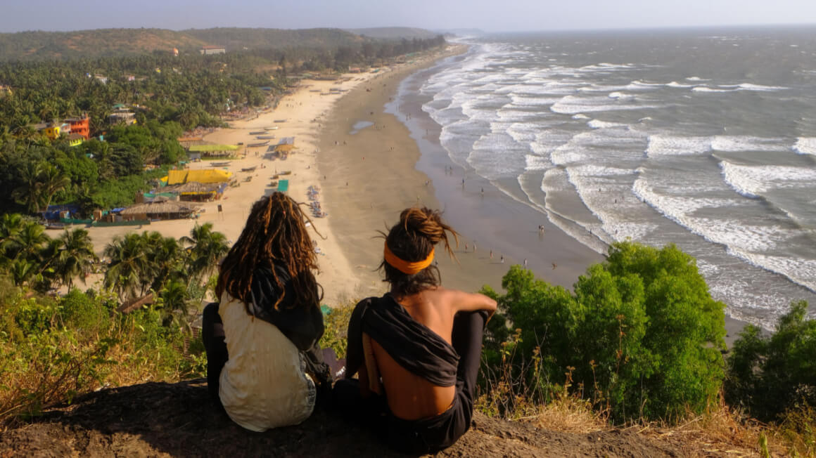 two guys sitting on a cliff overlooking a beach in india best hostel stories