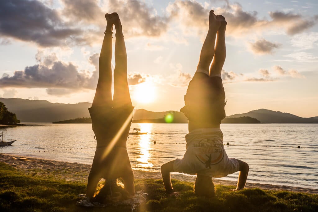 Two people doing a handstand on the beach in front of the sunset