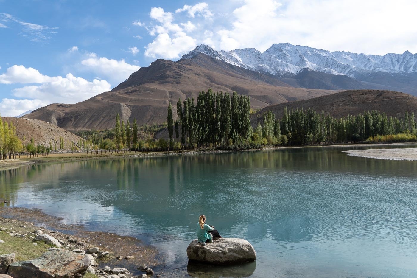 girl sitting on rock near bright blue river