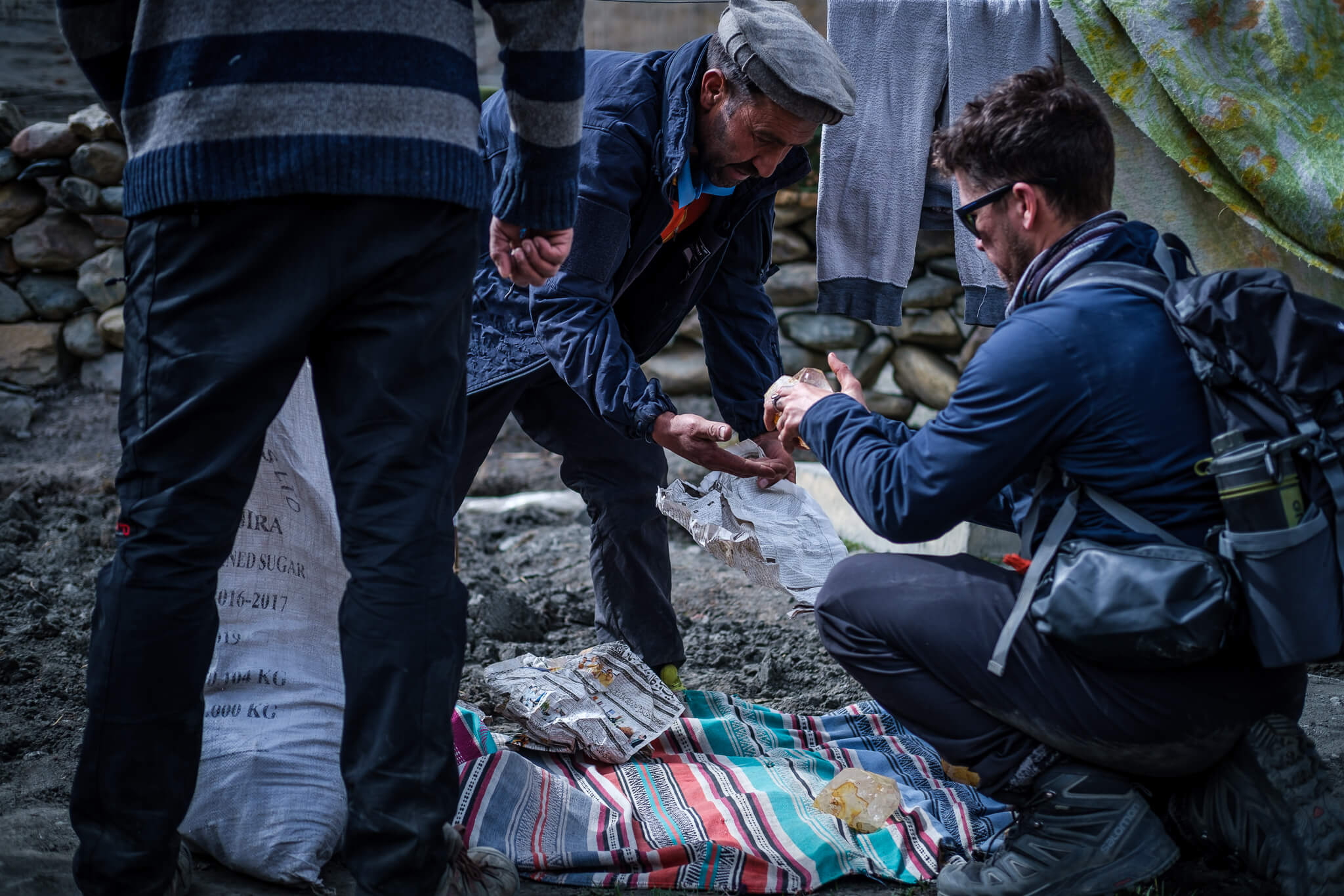 a Pakistani man selling to a tourist wearing boots and a backpack over a colourful blanket