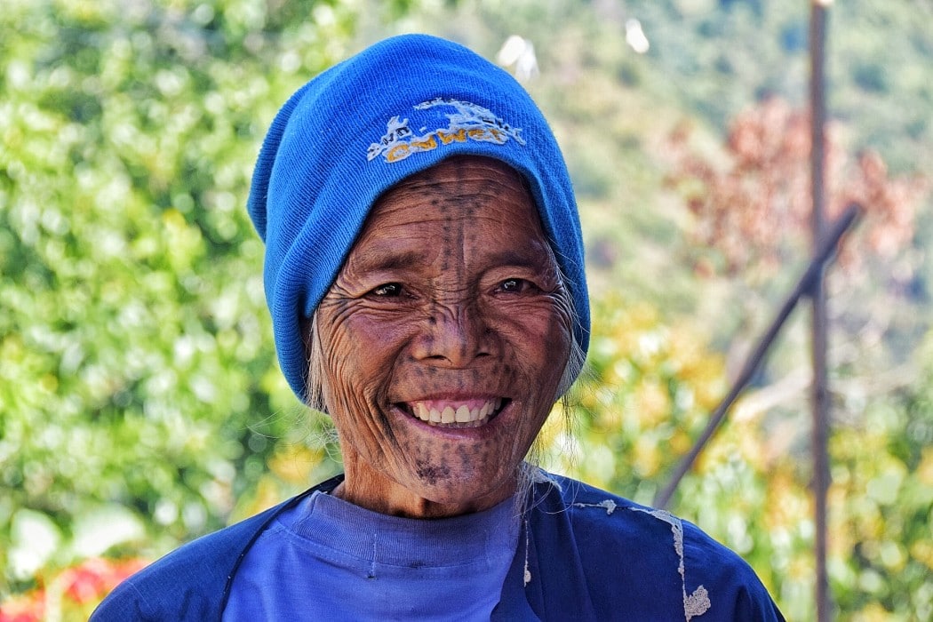 A smiling woman with face tattoos photographed while trekking in Myanmar