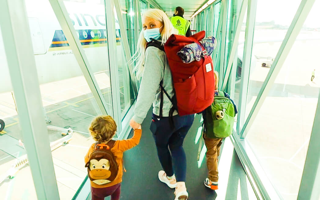 woman holding two kids hands boarding a plane