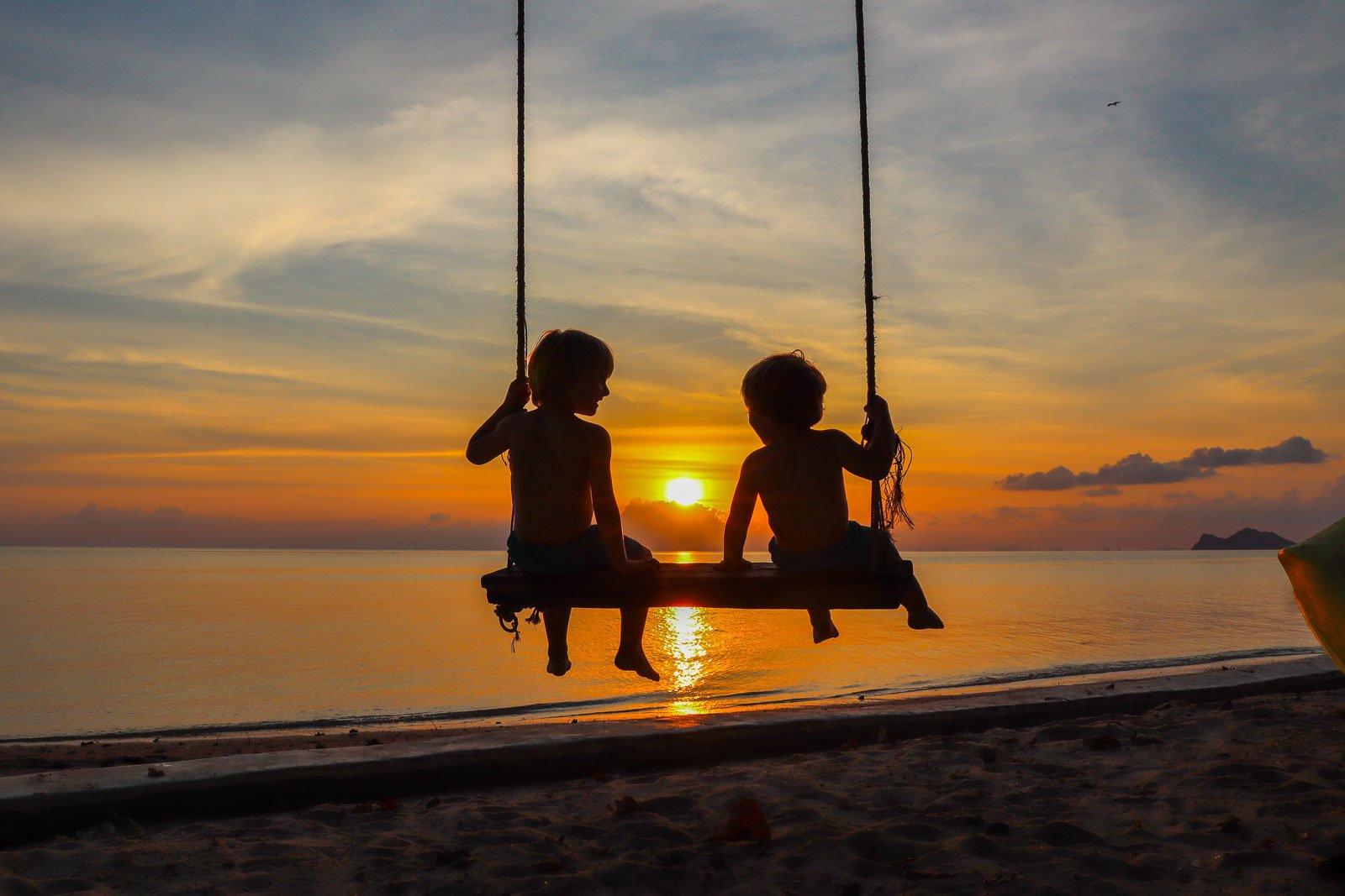 children on a wooden swing with an incredible bright orange beach sunset in front of them