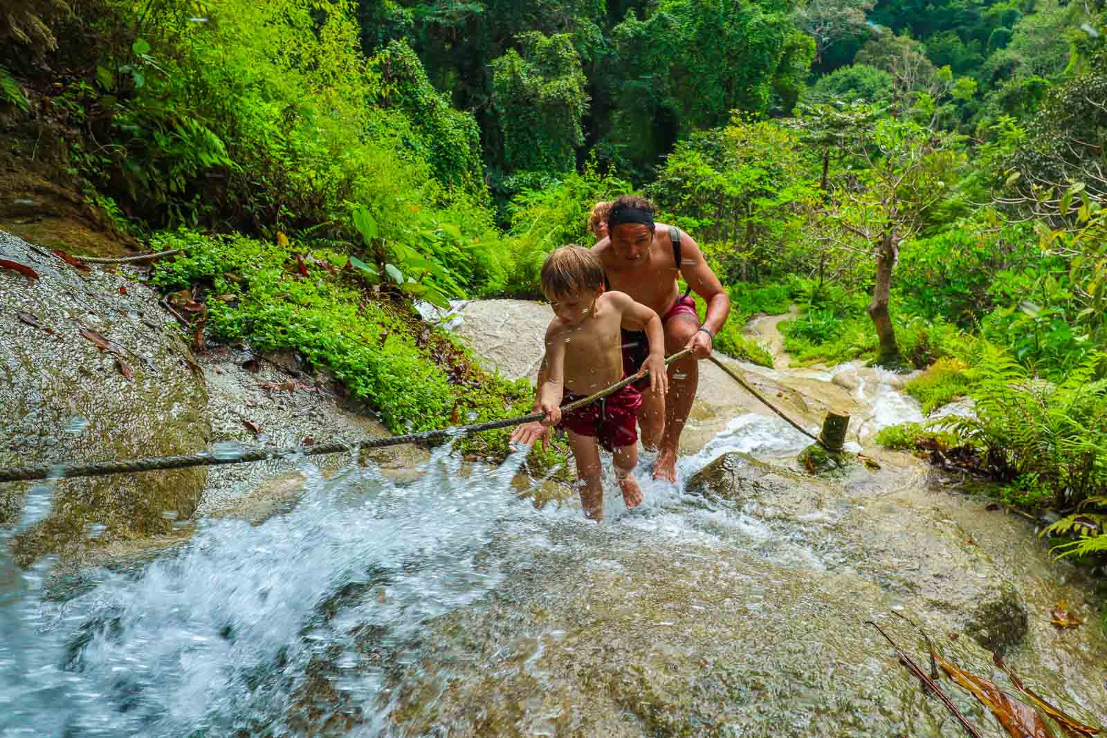 small child and father climbing a waterfall with a rope