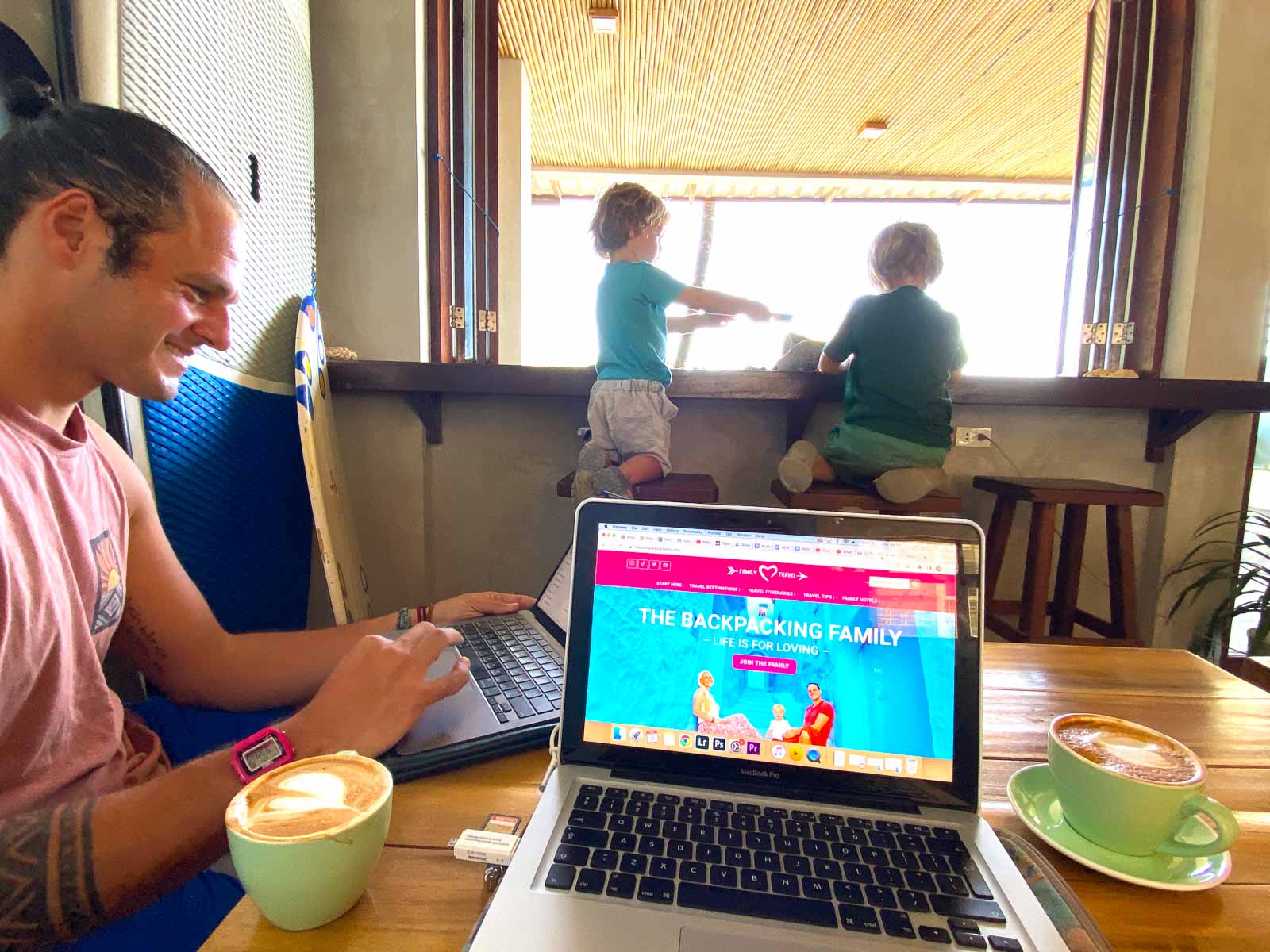 man working on a laptop at a coffee shop while backpacking with kids