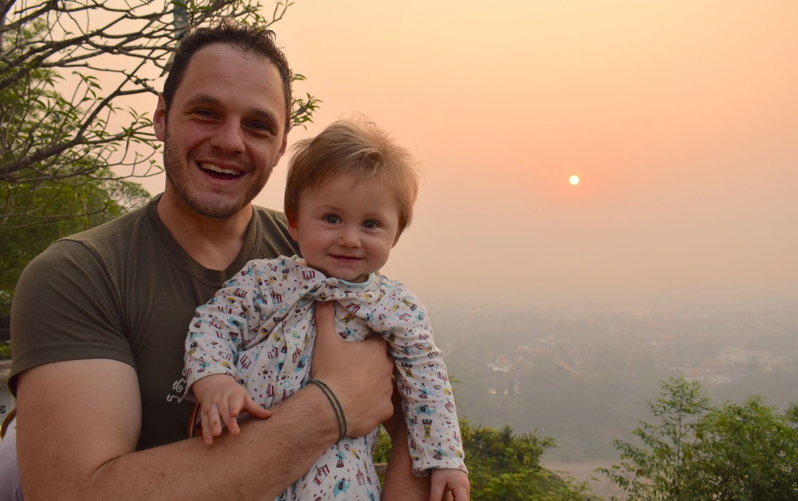 man holding a child in front of an orange sunrise in laos full time family travel