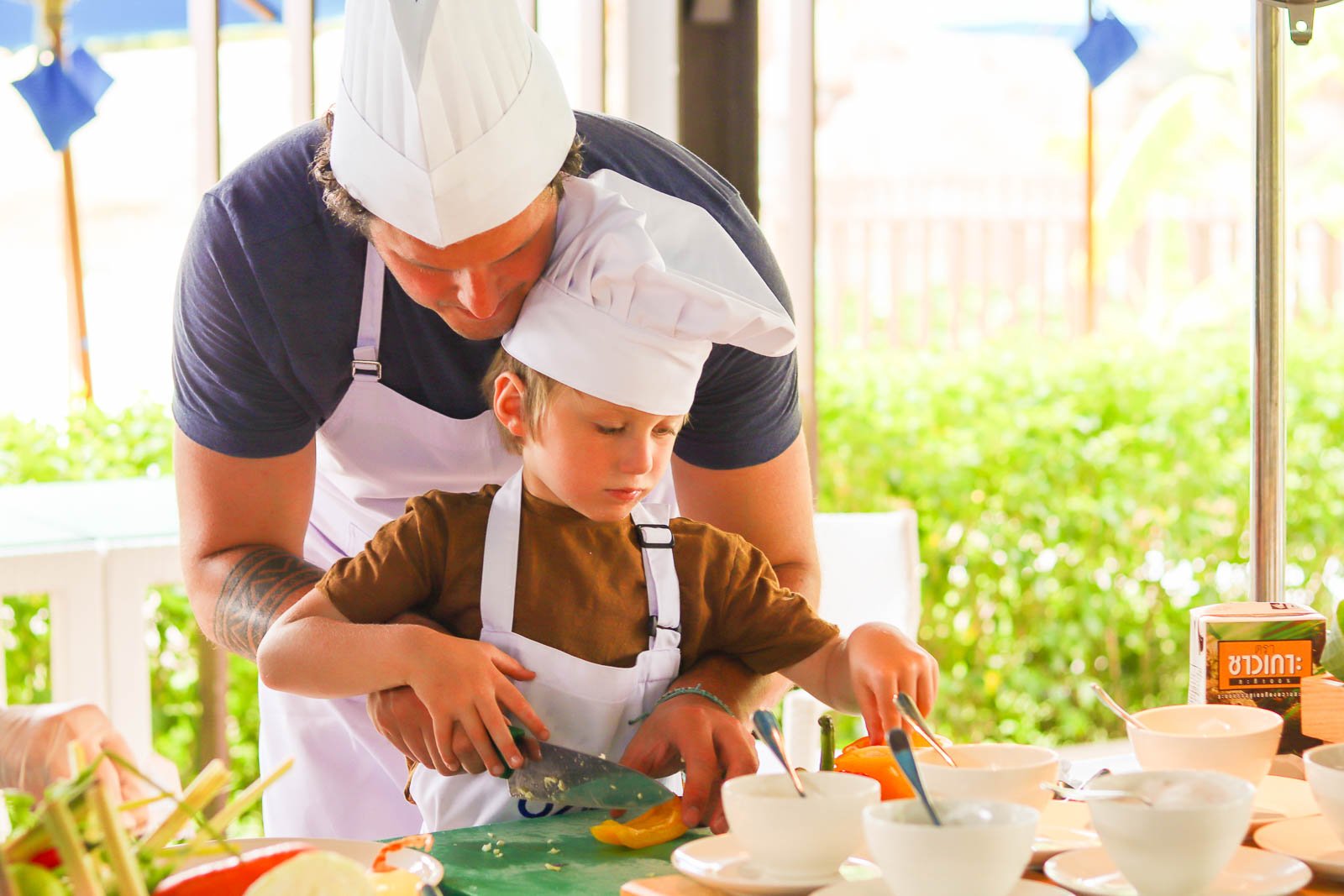 kid in white chef hat learning to cook a dish with his father