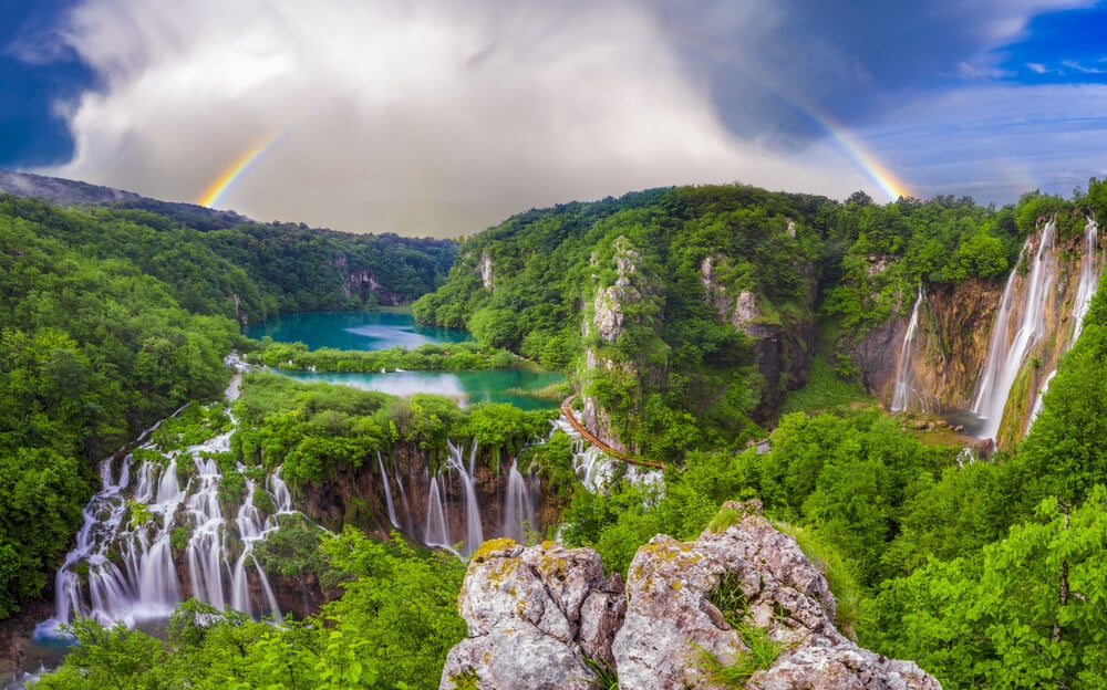 a rainbow over the many emeralnd colored cascades of plitvice falls