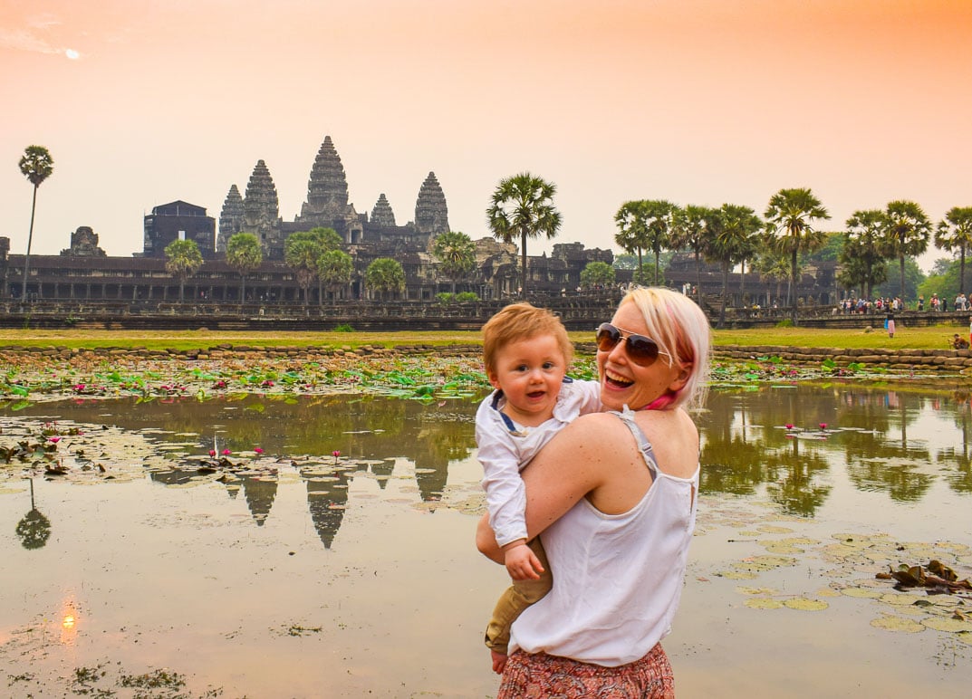 woman holding a baby at angkor wat with an orange sunrise behind her