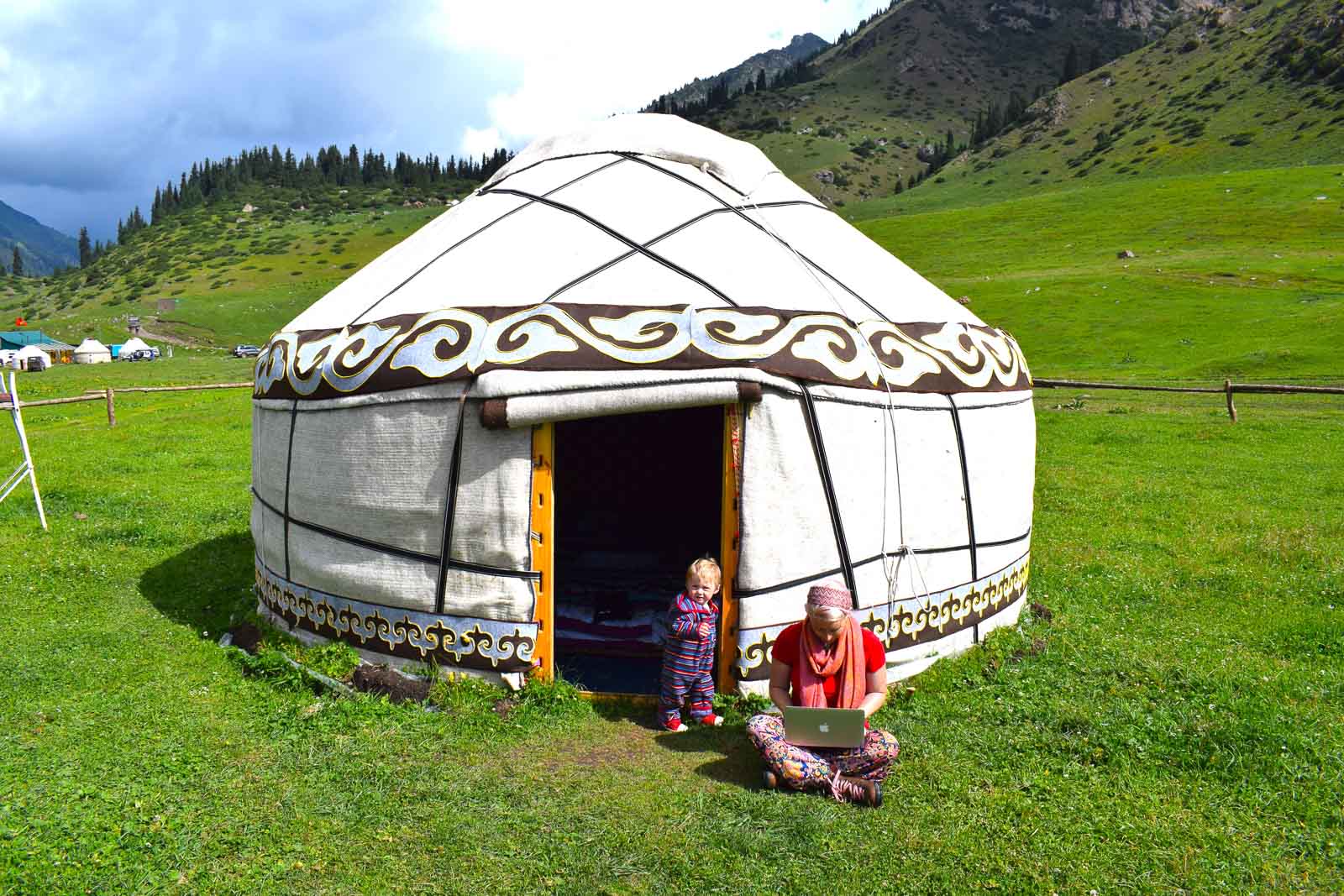 mom working on a laptop in the grass outside of a white yurt in kyrgyzstan