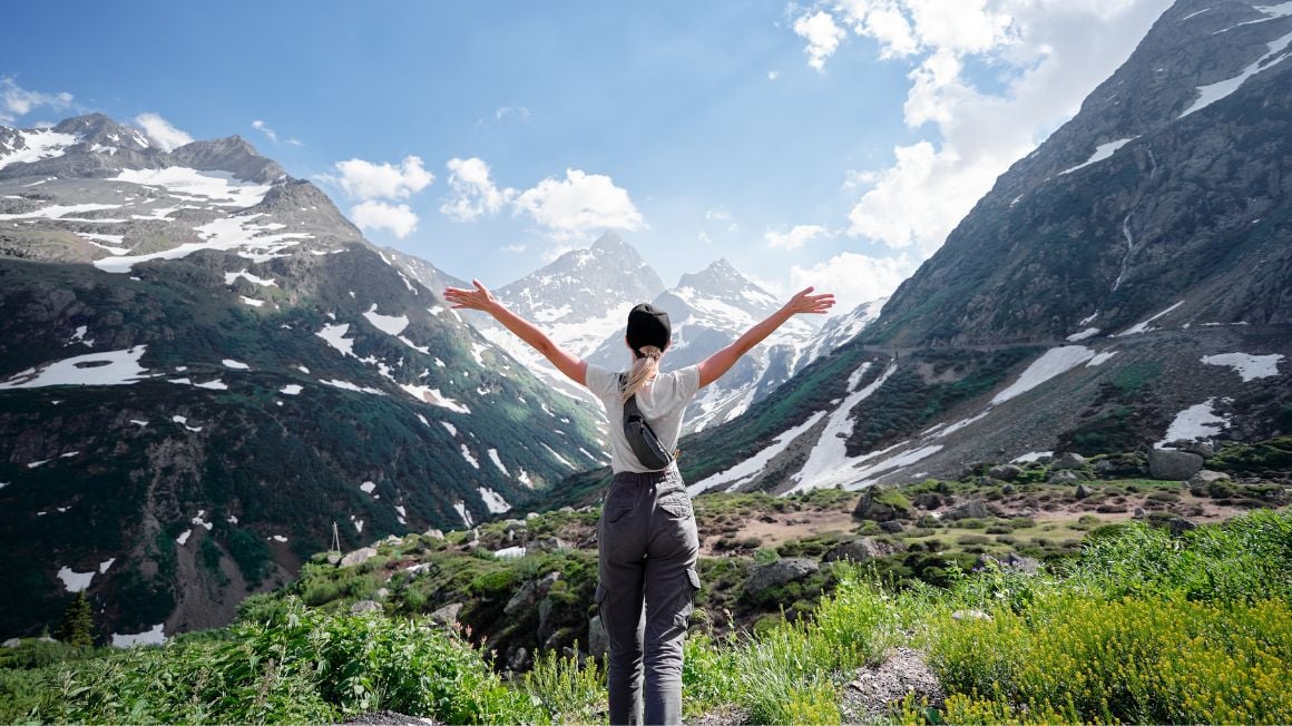 girl traveler hiking with hands up in the swiss alps