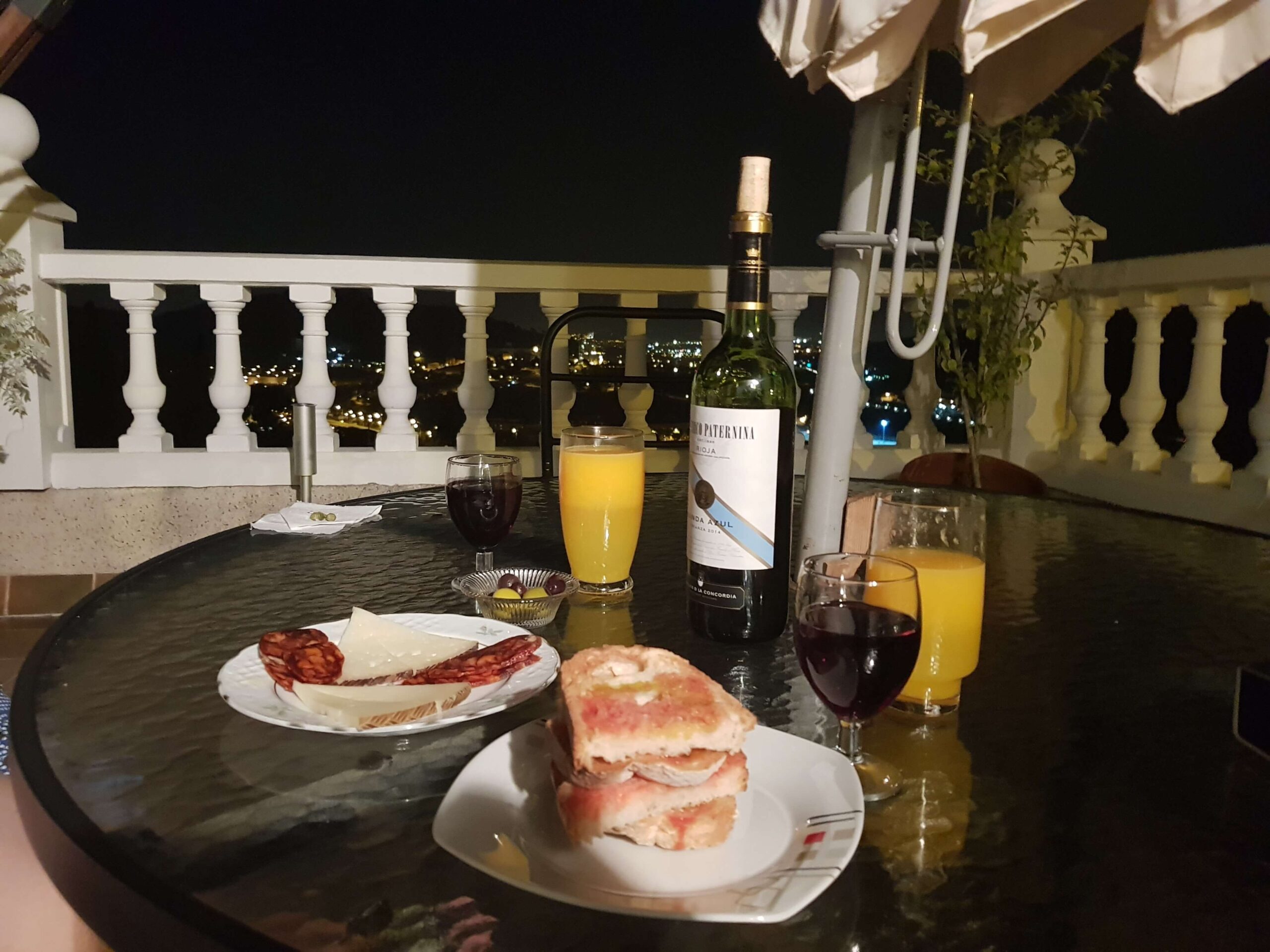 Traditional Spanish Tapas with orange juice and red wine served on a balcony with city views at night