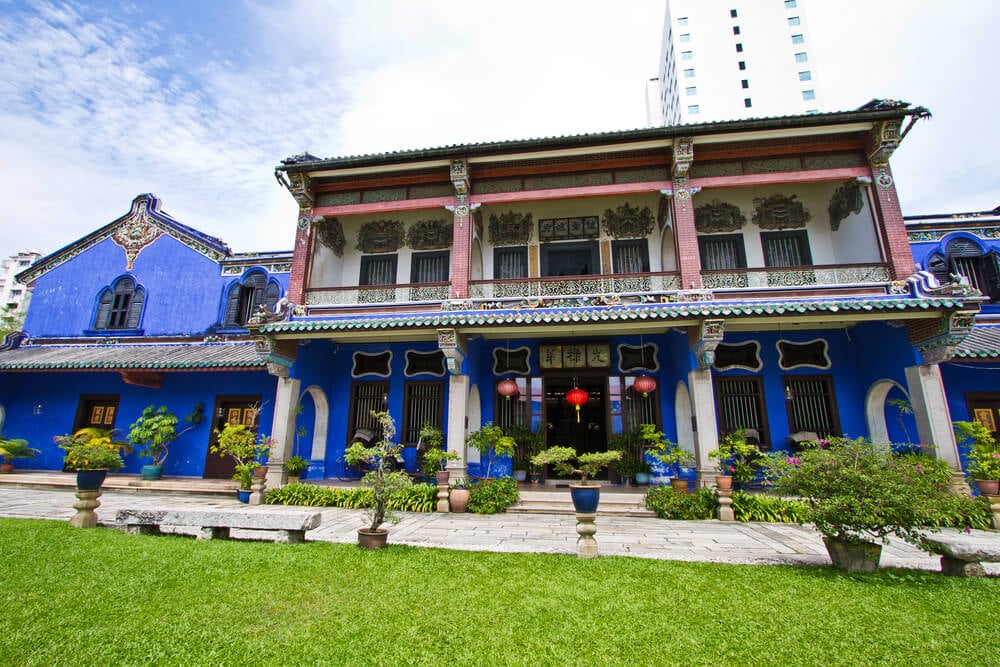 a bright blue colored mansion with red accents in penang malaysia with green grass and plants in front of it