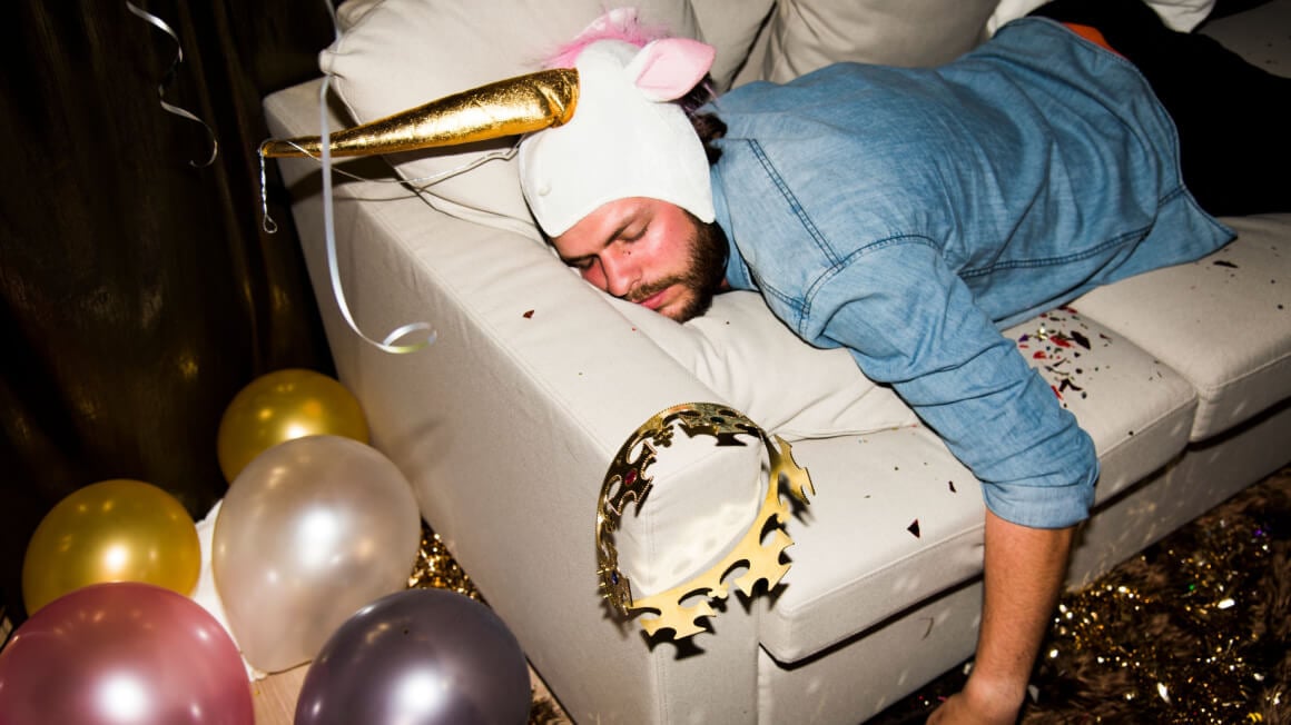 Man with unicorn hat passed out on a sofa