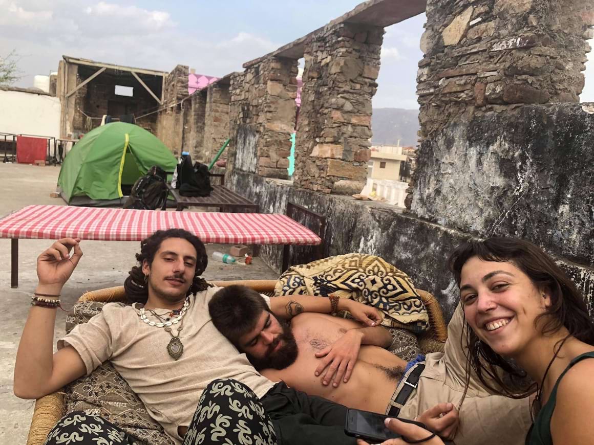 three people lounging on a charpai hammock on a rooftop while staying at a hostel in india