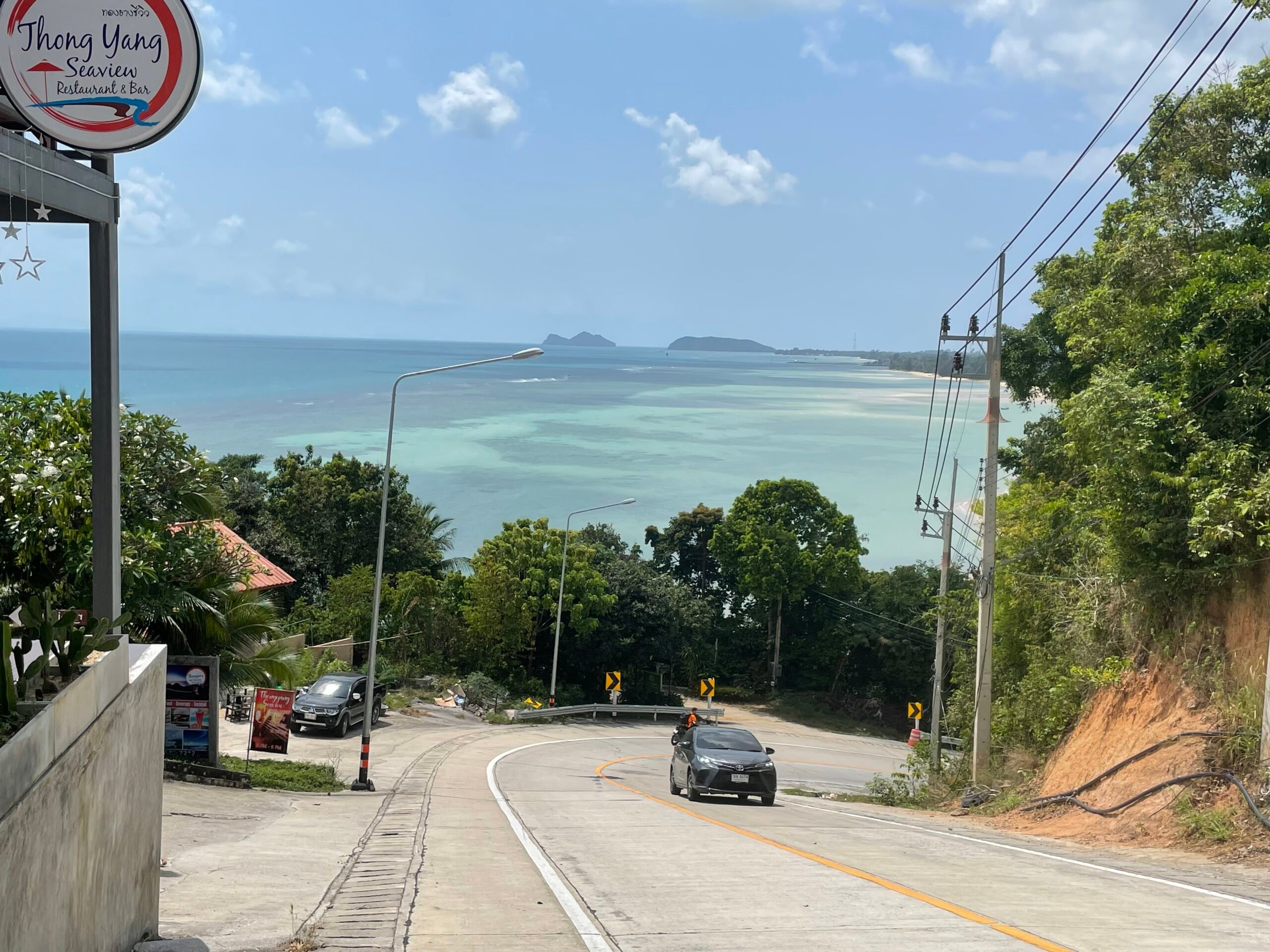 a car driving a up a steep road with a huge bright blue ocean behind it on koh phangan