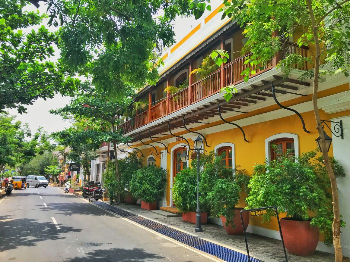 yellow building with a charming wooden balcony and lush greenery in Pondicherry's French Quarter.