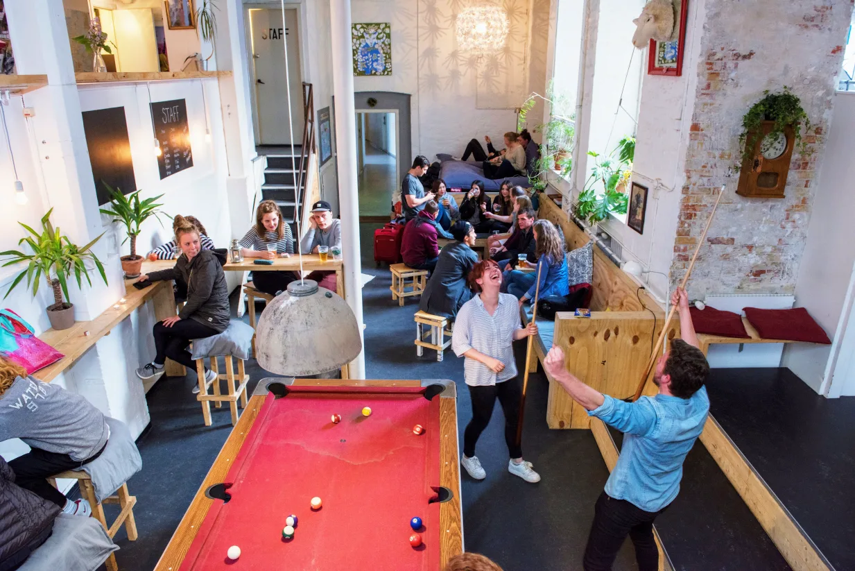 hostel guests playing pool in a well lit common room