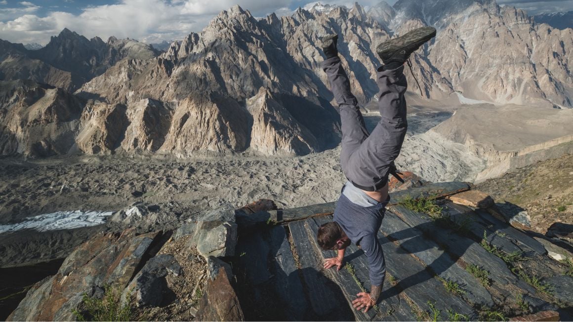 man doing a handstand while on a high altitude trek in the mountains