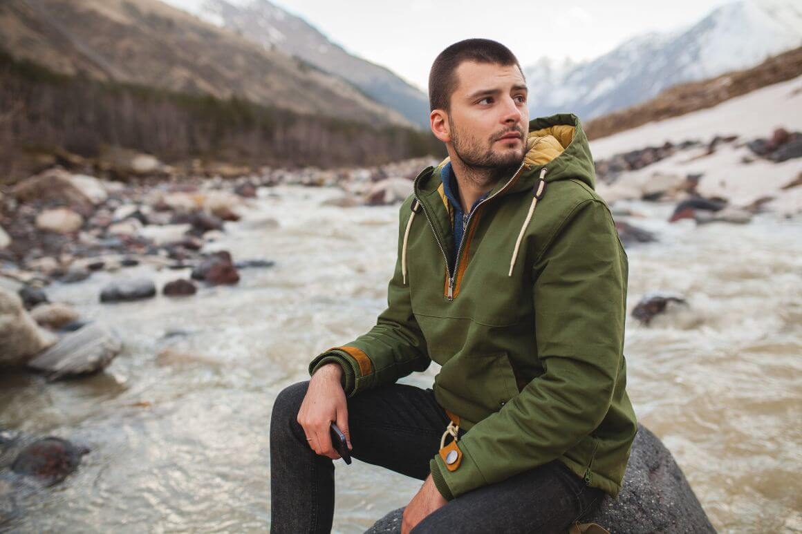 man sitting on a rock by a river holding a smartphone