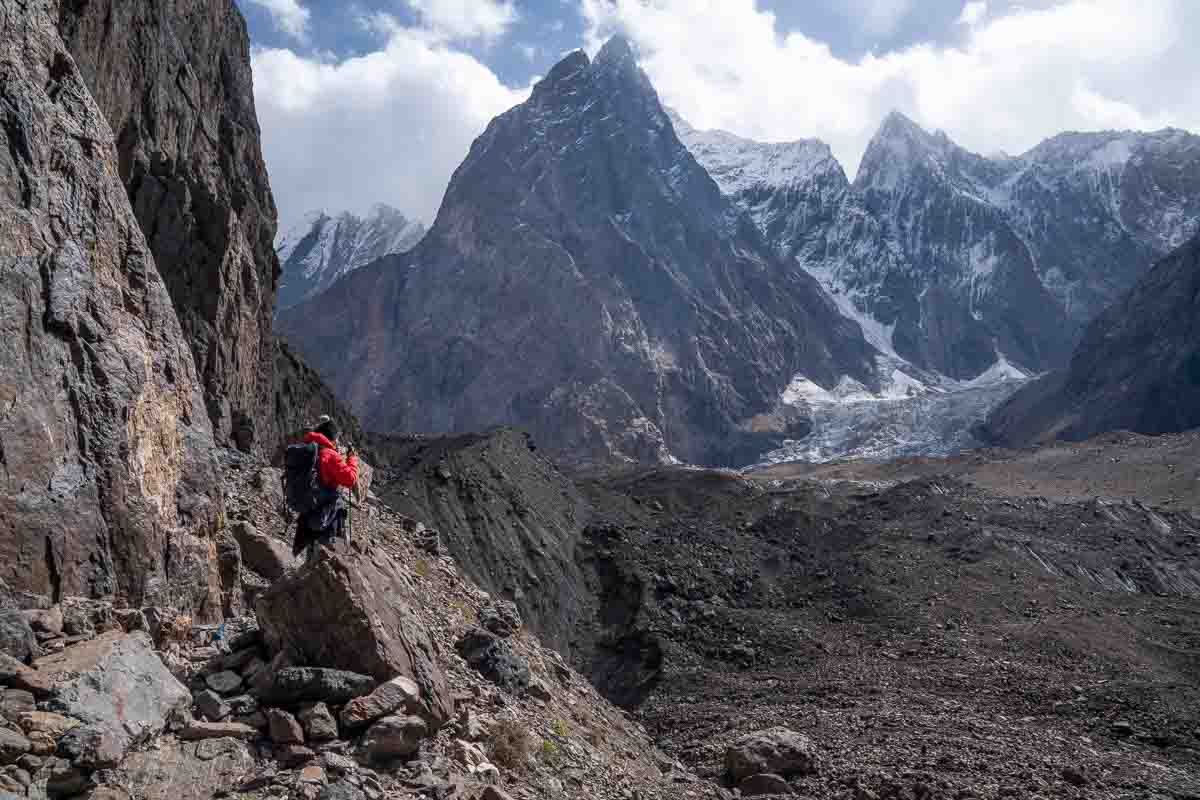 girl in red jacket standing on a rocky cliff looking out at massive glaciers while hiking in pakistan