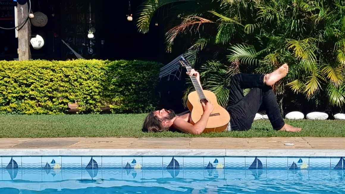 a man playing guitar by a swimming pool at a hostel in Brazil
