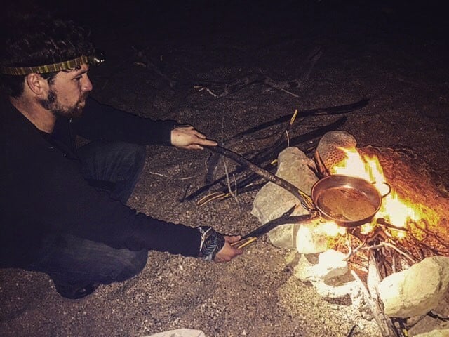 man cooks under the fire while camping out in nature