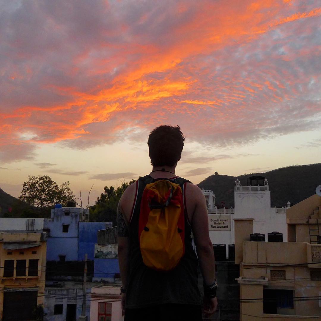 A person standing looking out over a local town in Iran as the sun sets in the distance