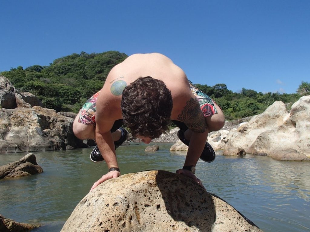 A man doing calisthenics fitness training on a rock next to a small lake.