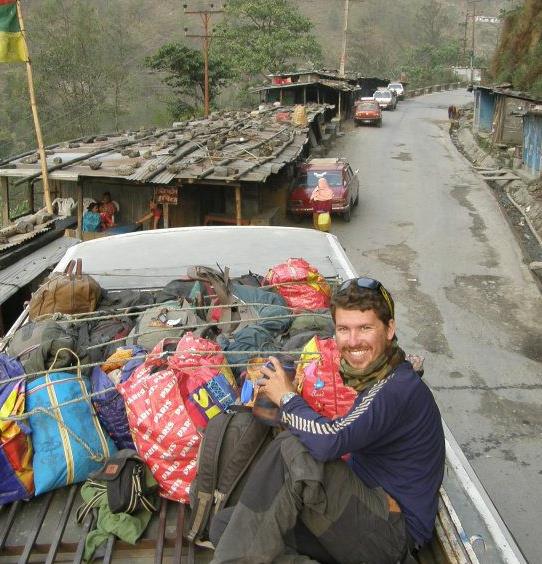 backpacker will sitting on top of a loaded bus while hitchhiking in nepal