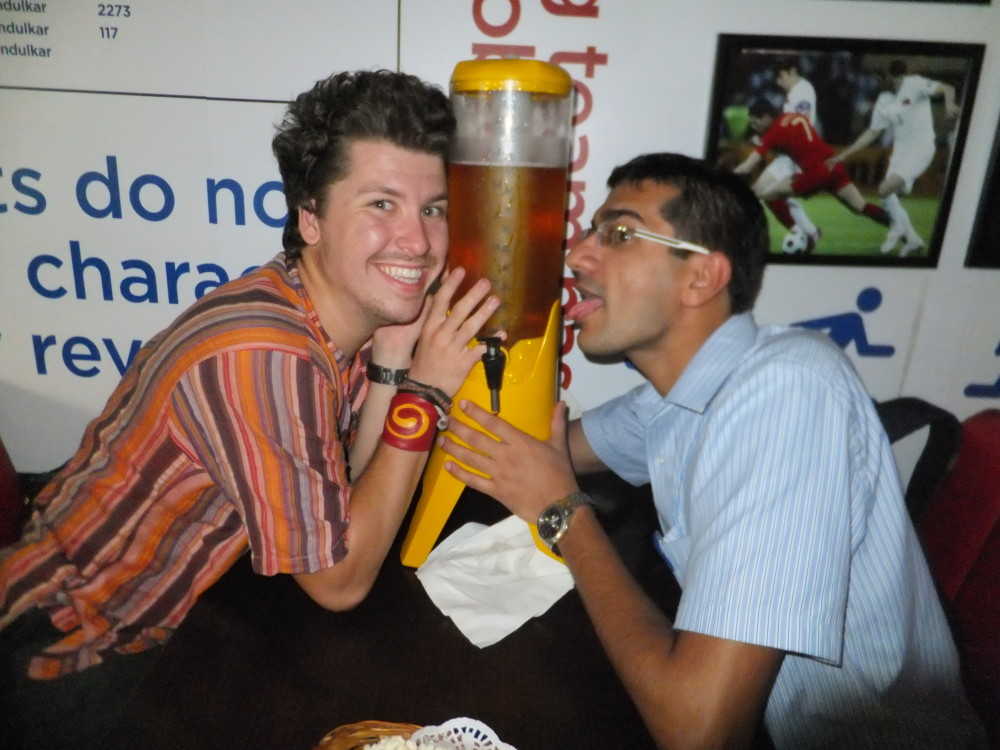 Two men hug a massive container with a tap at the bottom full of beer and look a little drunk