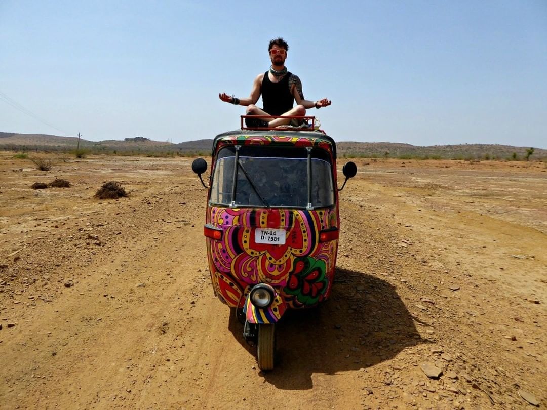 man sitting on top of a multicolored autorickshaw on an offbeat adventure in the Indian desert