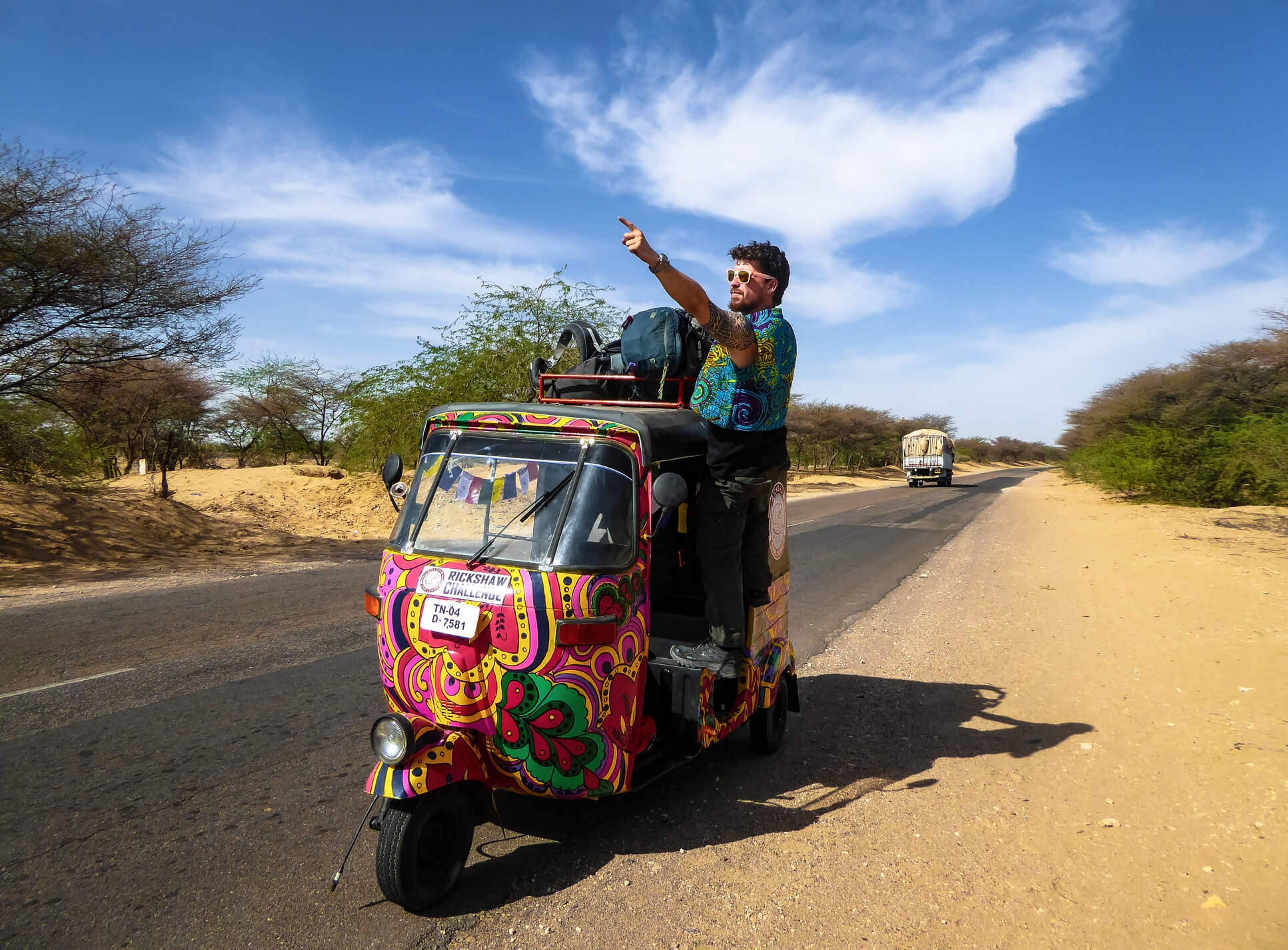 man hanging out of a psychedelic colored rickshaw in the desert of india