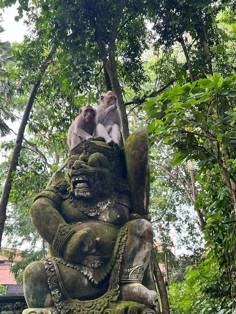 Two monkeys are perched atop a traditional Balinese statue in the Monkey Forest, Ubud, Bali, Indonesia.