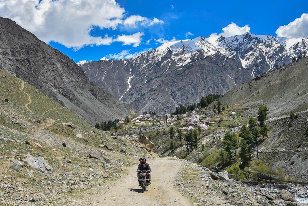 pakistan adventure tours men riding a motorbike on a dirt village road