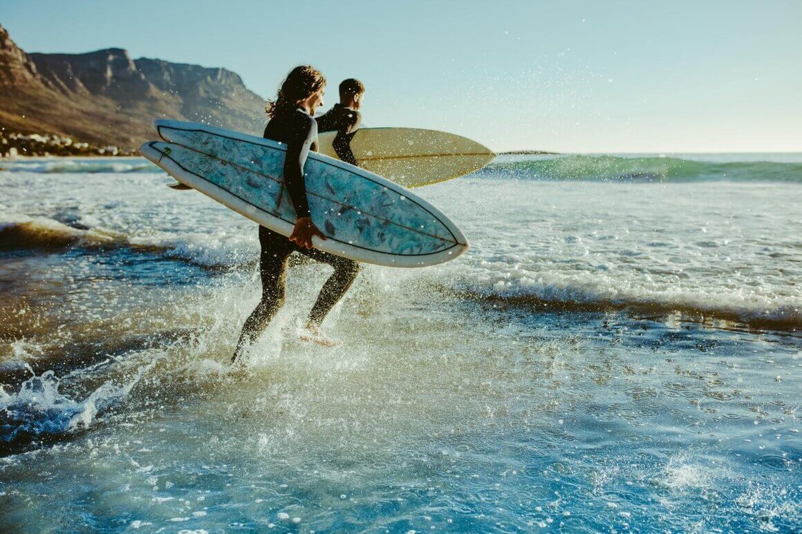 surfers on the beach running towards the water with their surfboards