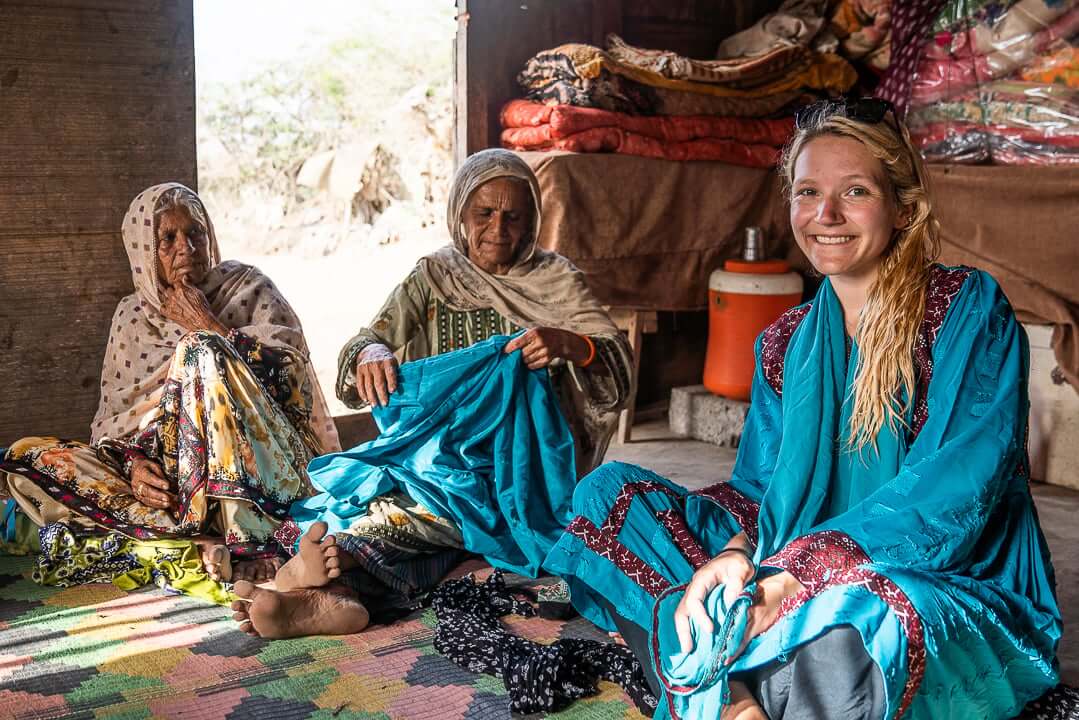 Samantha is sitting in colourful clothing in a traditional house with two women in a village in Pakistan